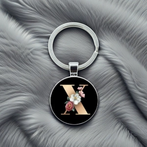 Close-up of silver keychain with letter X and floral patterns on black background