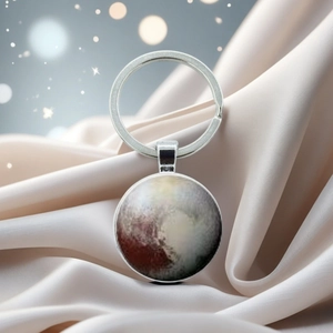Macro detail of planet Pluto crystal glass keychain on luxury champagne silk fabric