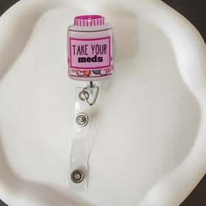 Detail view of pink pill bottle retractable badge holder with Take Your Meds text