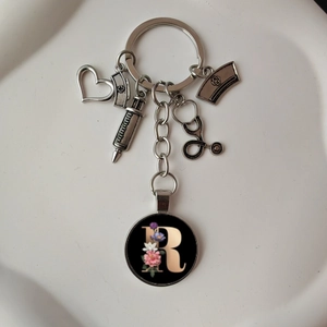 Detail of medical keychain with silver charms and floral letter R on a white background