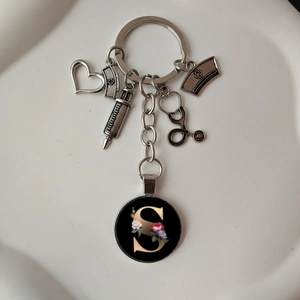 Detail of medical keychain with stethoscope, nurse hat and floral letter S charm