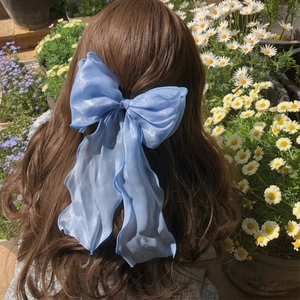 Light blue organza bow hair clip with long tassels worn on wavy brown hair outdoors