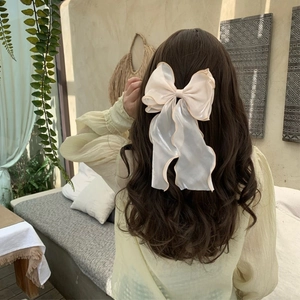 Elegant oversized cream bow hair clip with wavy edges on a brunette model's hair