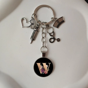 Detail of medical keychain featuring silver stethoscope syringe charms and floral letter W