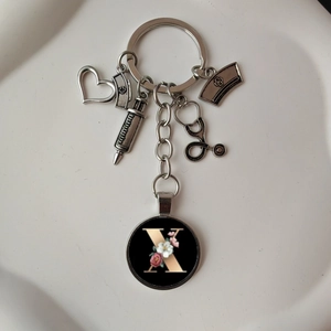 Macro detail of silver medical keychain with syringe, heart, and floral letter X pendant