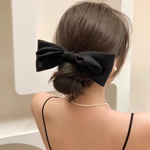 Dettaglio di un grande fiocco in raso nero per capelli indossato su uno chignon basso