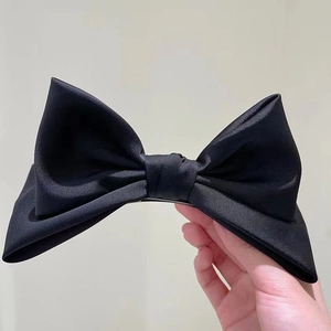 Dettaglio di un grande fermaglio per capelli a fiocco in raso nero con molla in metallo