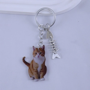 Close-up of orange cat acrylic charm with silver fishbone pendant on a metal keychain
