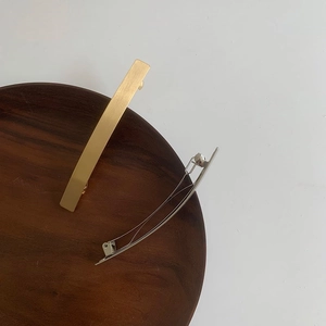 Minimalist gold and silver alloy spring hair clips displayed on a dark wooden tray