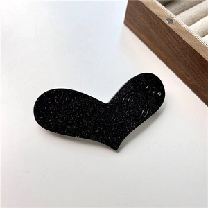 Gros plan d'une pince à cheveux cœur noire en acétate avec paillettes et gravure