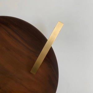 Detailed view of matte gold brushed metal hair clip on a dark walnut wood base