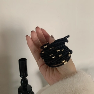 Elastic hair ties in black with gold metal connector held in hand against beige background