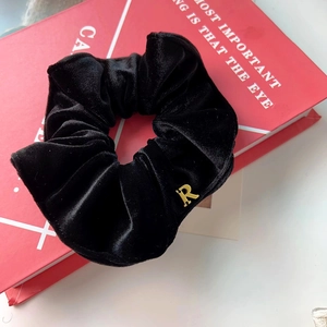 Détail d'un chouchou en velours noir avec un pendentif lettre R dorée sur livre rouge