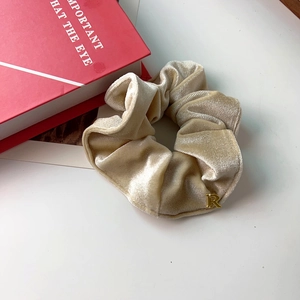 Détail d'un chouchou en velours champagne avec un pendentif en métal doré lettre R