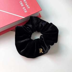 Chouchou élégant en velours noir avec un pendentif lettre R doré sur une surface blanche