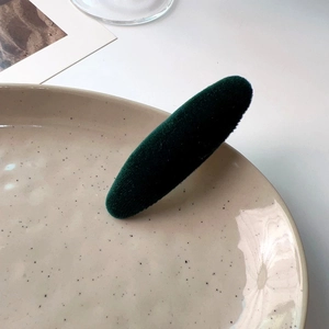 Close-up of a vintage dark green velvet hair clip on a minimalist ceramic plate