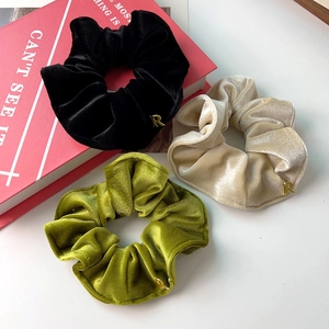 Gros plan de chouchous en velours noir, doré et vert avec des breloques en métal R
