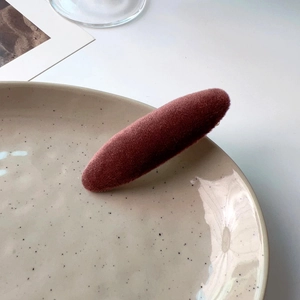 Detail view of a burgundy velvet duckbill clip on a ceramic plate with soft lighting
