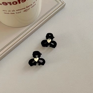 Close-up of two mini black velvet bow hair claws with gold heart detail on a fabric surface