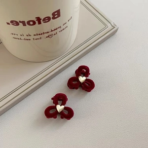 Pair of burgundy velvet bow hair claws with gold heart detail on a textured surface