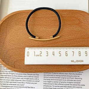 Detailed view of elastic hair tie with 4.5cm matte gold metal bar on wooden tray