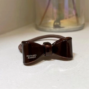 Close-up of brown bow hair tie with Creation France letter print on elastic band