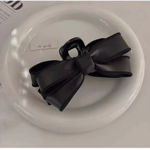 Elegant black leather bow hair claw clip for women on a white minimalist background