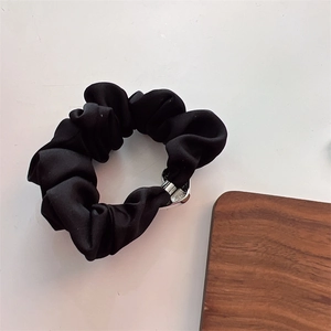 Detail of black satin hair scrunchie with a silver metal ring accent on a white desk