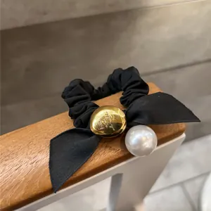 Détail d'un chouchou noir avec breloque dorée lettrée et pendentif perle blanche