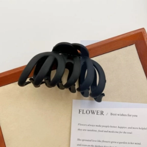 Close-up of a large matte black hair claw clip with sleek curved lines on a vintage card