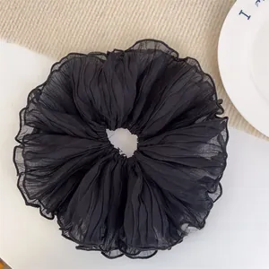 Close-up of a large black ruffled chiffon scrunchie on a white surface with knit texture