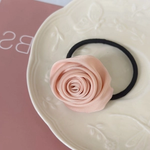 Detail of pink satin rose hair tie with black elastic band on white ceramic plate