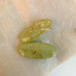 Dettaglio di fermagli ovali in resina verde chiaro con scaglie dorate e clip metallica
