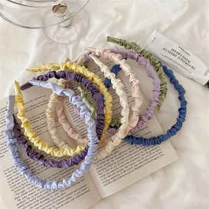 Close-up of pleated satin headbands in multiple pastel colors arranged on a book