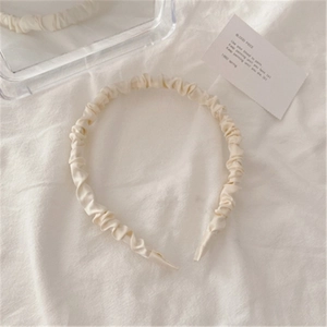 Close-up of cream pleated satin headband with elegant ruching on a soft textured background