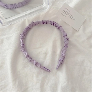 Close-up of lavender purple ruched satin headband with silky texture on white fabric