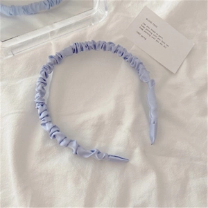 Close-up of a light purple pleated satin headband displayed on a minimalist white fabric