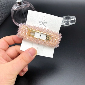 Nahaufnahme der rosa Kristall-Haarklammer auf weißer Karte, elegant von Hand gehalten