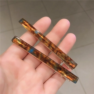 Close-up of two amber patterned rectangular hair clips with gold metal base