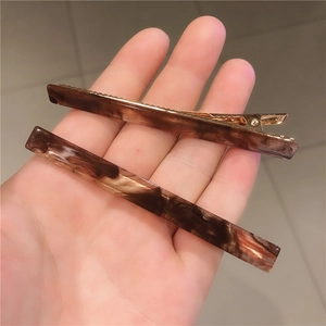 Detail showing marble texture hair clips and golden metal duckbill mechanism for secure grip