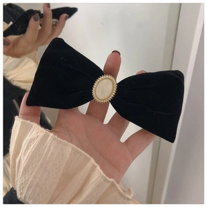 Detail of a large black velvet bow hair clip featuring a pearl-encrusted oval centerpiece