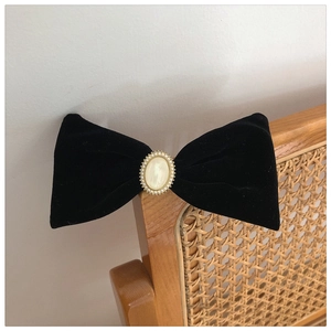 Close-up of elegant black velvet bow hair clip with central pearl and vintage metal trim