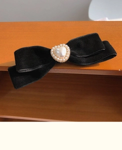 Macro detail of black velvet bow hair clip with heart-shaped pearl center decoration