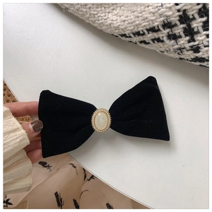 Close-up of black velvet bow hair clip with central pearl and golden bead trim detailing