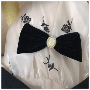 Close-up of velvet bow hair clip with central pearl gemstone on floral fabric