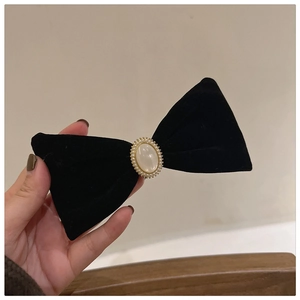 Detailed view of a black velvet bow hair clip with an elegant faux pearl and gold beads