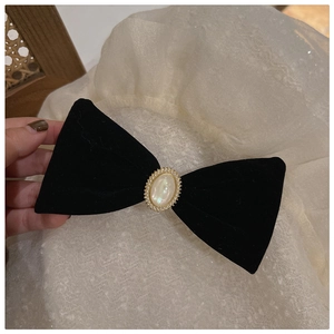 Close-up of black velvet bow hair clip with central pearl and golden bead trim details