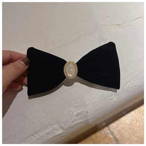 Close-up of French velvet black bow hair clip with central pearl and golden trim details