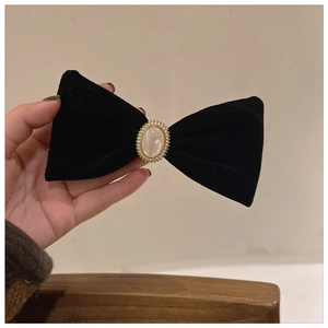 Detail of elegant black velvet bow hair clip with faux pearl and gold bead accents