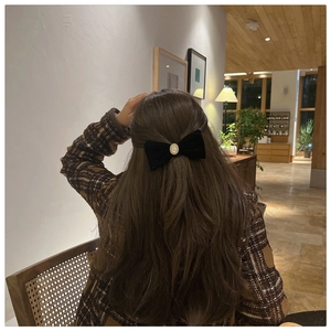 Close-up of a black velvet bow hair clip with central pearl on long wavy hair